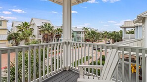 Un balcon doté d’une balustrade blanche, donnant sur un quartier résidentiel avec des maisons et des palmiers.