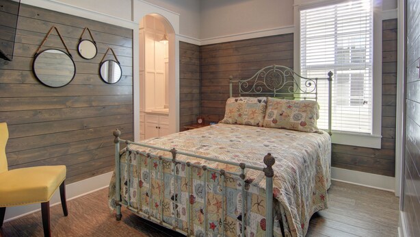 A bedroom with a bed, a chair, and a window with blinds. - Cajun Cottage 108 BE (Port Aransas)