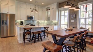 Una cocina amplia con armarios blancos, una isla grande con taburetes de bar, un refrigerador de acero inoxidable y una lámpara colgante.