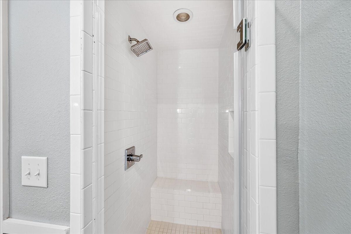 A shower with white tiles, a handheld showerhead, and a wall-mounted control panel.