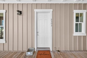A front door with a number, a welcome mat, and a basket. - By the Sea TC 2303 (Port Aransas)