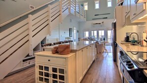 Une cuisine spacieuse dotée d’un îlot central, de meubles blancs et d’un escalier en bois.
