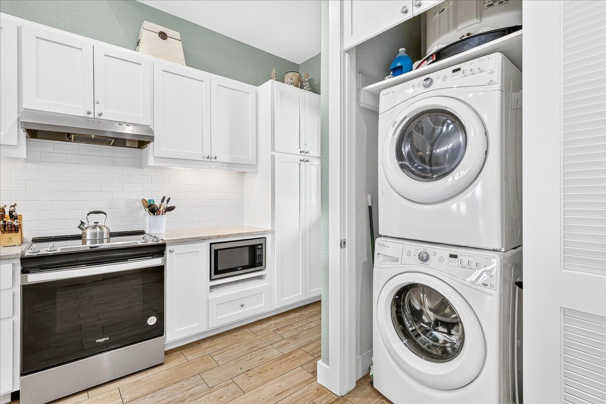 A kitchen with white cabinets, a microwave, a stove, and a stacked washer and dryer.