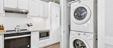 A kitchen with white cabinets, a microwave, a stove, and a stacked washer and dryer.