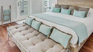 Une chambre spacieuse avec un grand lit, un banc rembourré, un éclairage suspendu et une peinture abstraite aux couleurs vives accrochée au mur.