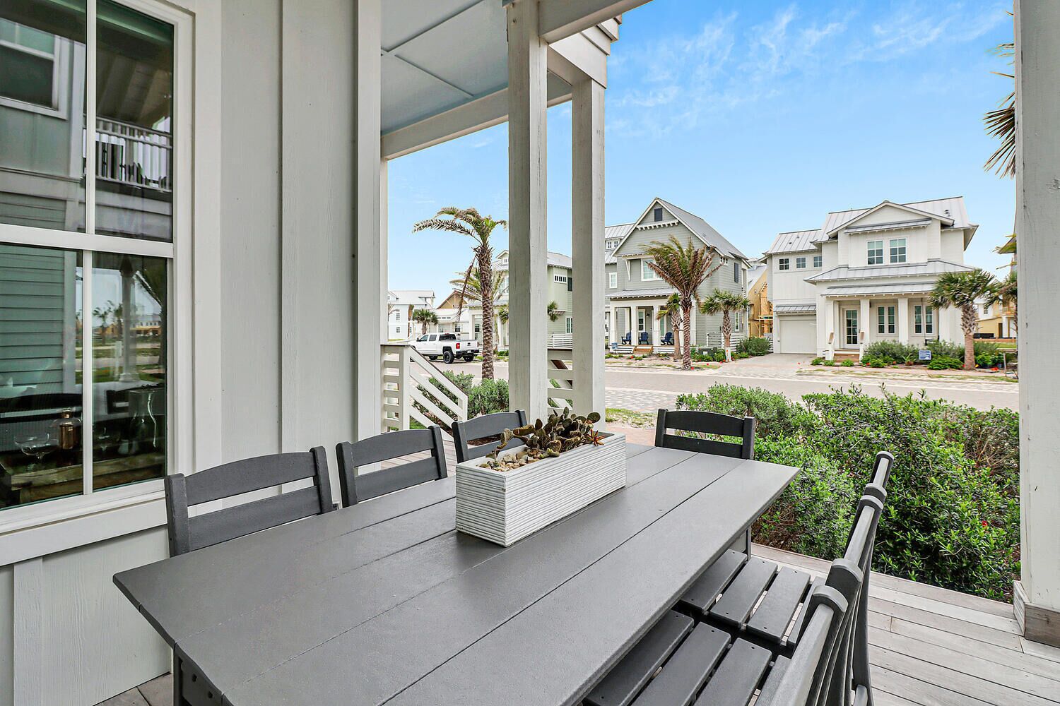 A covered patio with a table and chairs, a planter box with succulents, and a view of residential buildings.