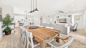 Una cocina amplia con una mesa de comedor de madera, sillas blancas, iluminación colgante y una isla grande.