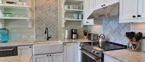 A kitchen with white cabinetry, a herringbone-patterned backsplash, a stainless steel range hood, and a granite countertop.