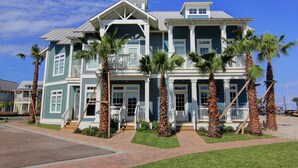 A two-story house with a balcony, a porch, and palm trees in front. - Island Time TC 4102 (Port Aransas)