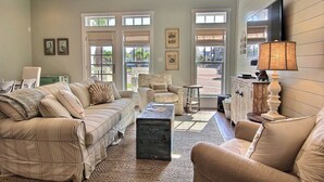 A spacious living room with a large sofa, a coffee table, and a television mounted on the wall. There are windows providing natural light and a view of the outside. - Island Time TC 4102 (Port Aransas)