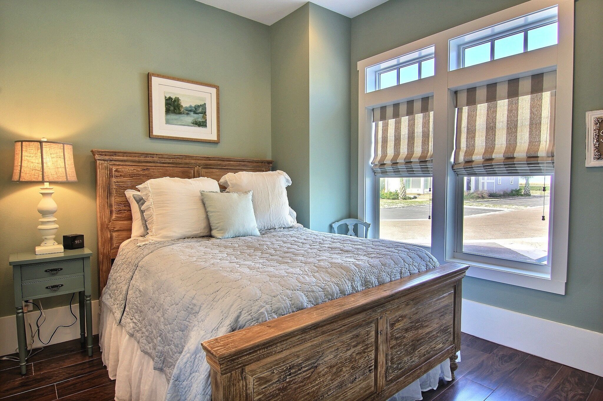 A bedroom with a wooden bed, a nightstand with a lamp, and a window with striped blinds.