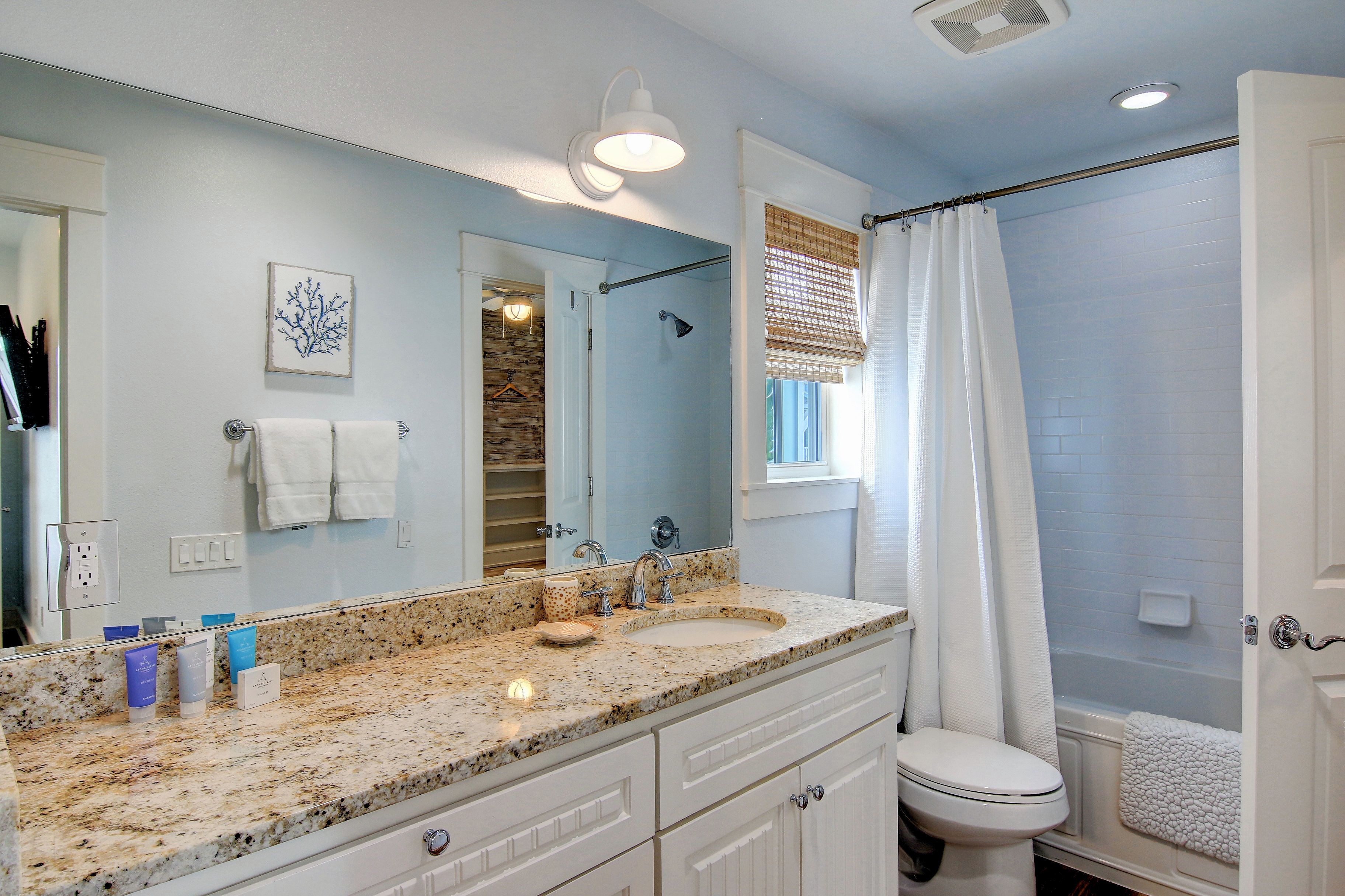 A bathroom with a granite countertop, white fixtures, a large mirror, and a shower area.