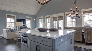 A spacious kitchen with a large island, dark wood flooring, and a high ceiling with exposed beams. - Coastal Charm 258 HI (Port Aransas)