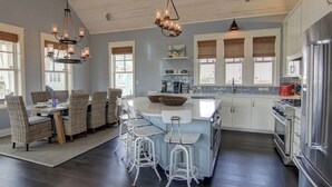 A modern kitchen with a central island, bar stools, and a dining area with wicker chairs. - Coastal Charm 258 HI (Port Aransas)