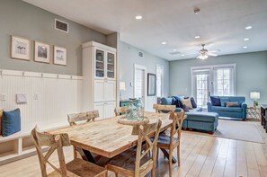 Een ruime woonkamer met een houten eettafel, een blauwe bank en een plafondventilator.