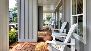 Une véranda couverte avec des fauteuils Adirondack blancs et une terrasse en bois.