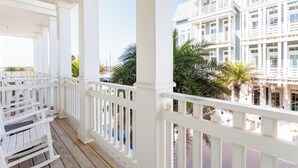 A covered porch with white railings and wooden benches, overlooking a beachfront property with white buildings and palm trees. - Dolphin Destiny TC 5102 (Port Aransas)