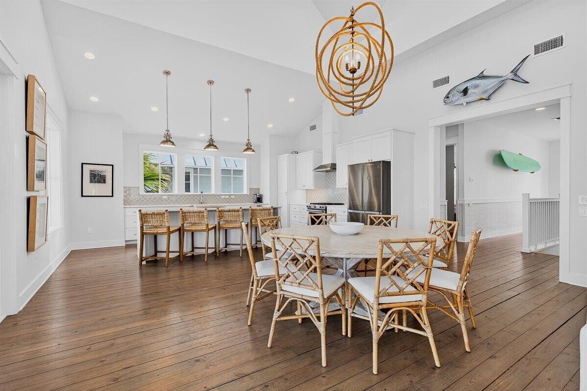 A spacious kitchen with white cabinetry, a large island, and a dining area with wicker chairs.