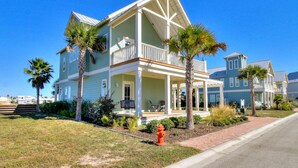 A two-story house with a balcony, surrounded by palm trees and a brick pathway. - Hip Nautic 113 WI (Port Aransas)