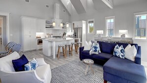 A spacious living area with a large blue sofa, white armchairs, and a kitchen island. - Hip Nautic 113 WI (Port Aransas)