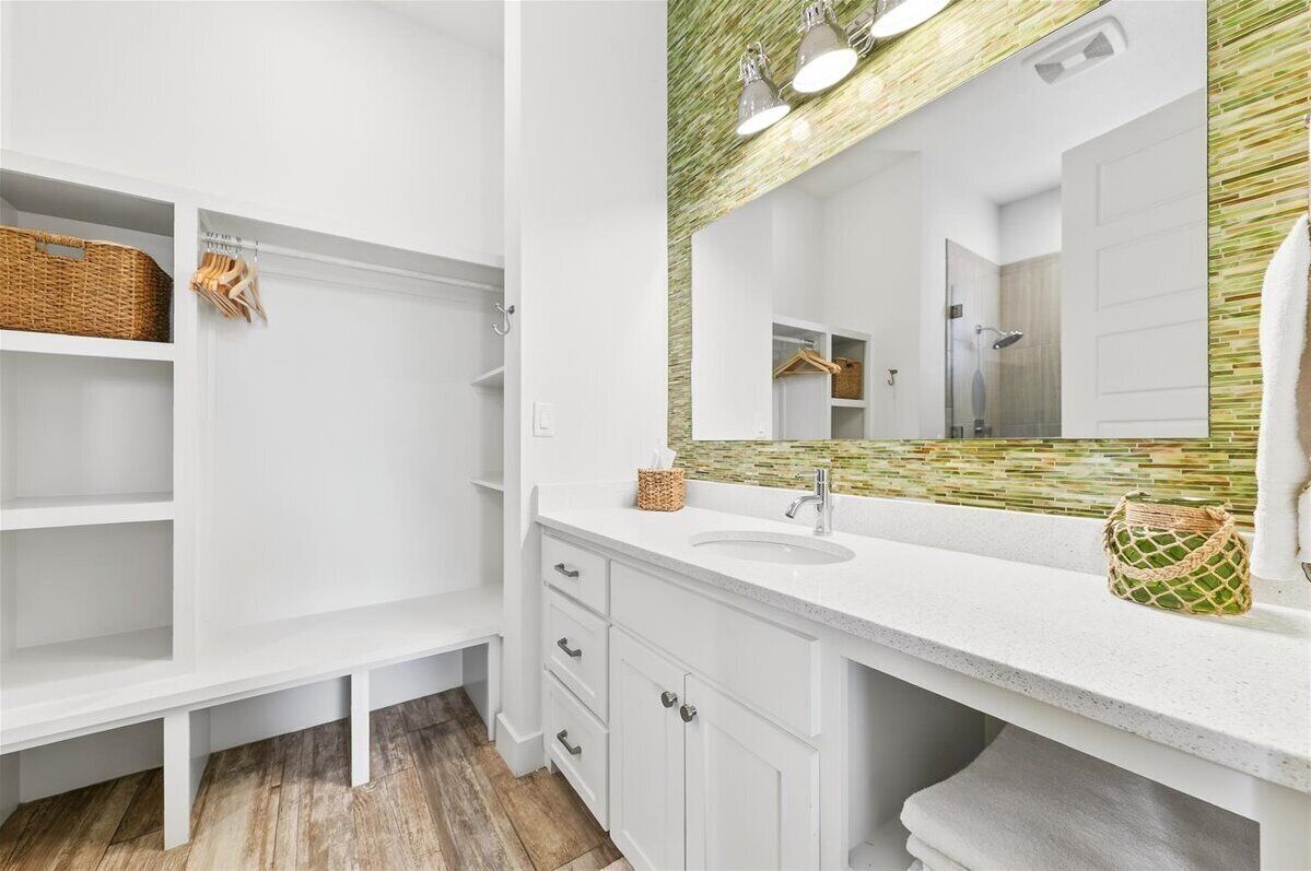 Une salle de bain avec des meubles blancs, un grand miroir et un pare-chocs en mosaïque verte.