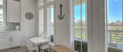 Une cuisine lumineuse avec des meubles blancs, une table à manger en bois et une grande fenêtre donnant sur des maisons.