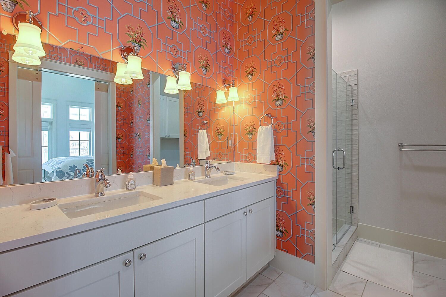 Une salle de bain moderne avec un grand miroir, des meubles blancs et un mur orné d’un motif.