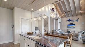 Une cuisine moderne dotée d’un plan de travail en granit, d’appareils électroménagers en acier inoxydable et de luminaires suspendus.
