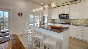 Une cuisine moderne avec des meubles blancs, un grand îlot central doté de tabourets, un four à micro-ondes et une cuisinière.