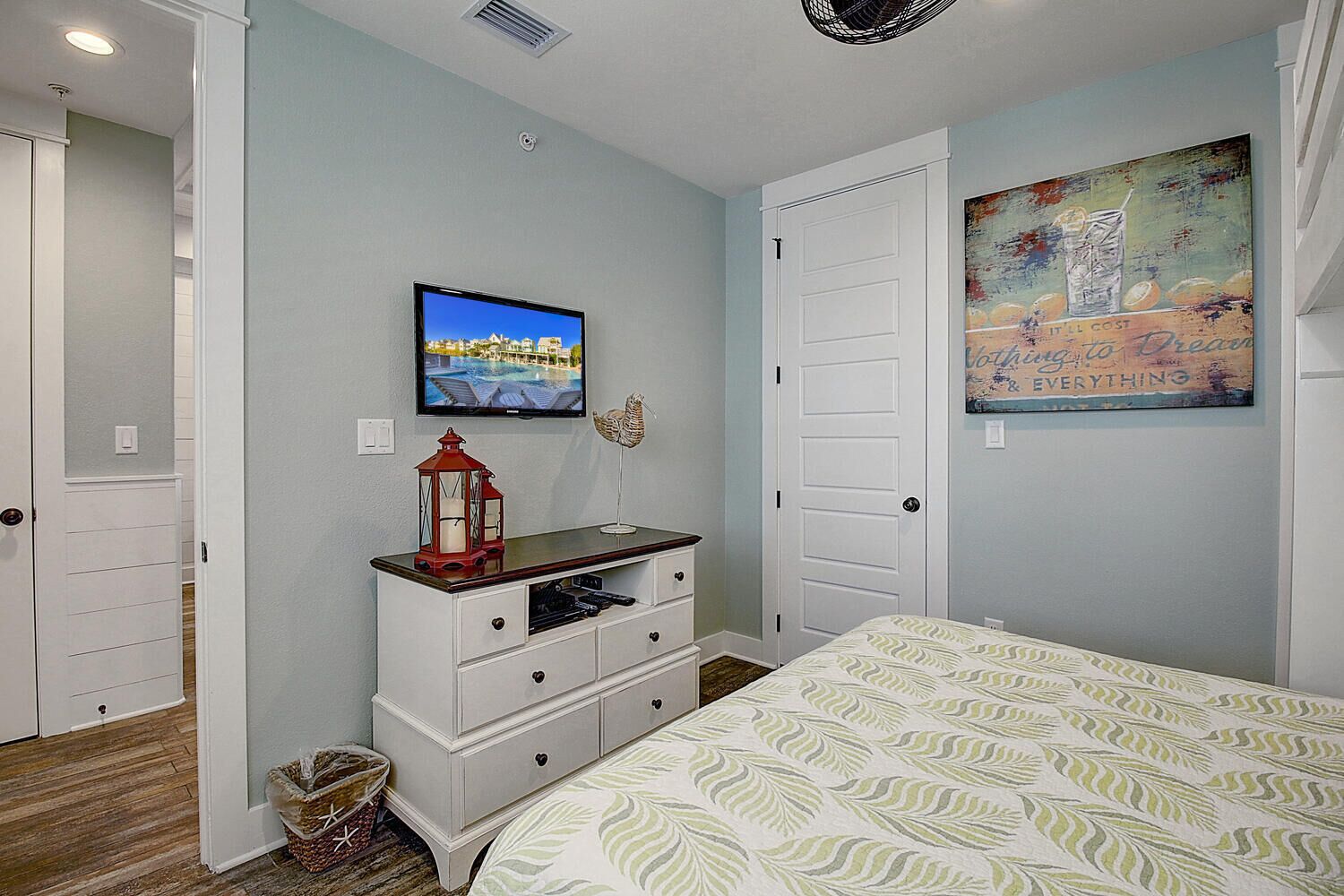 A bedroom with a bed, a TV, a dresser, a painting, and a door.