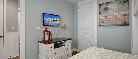 A bedroom with a bed, a TV, a dresser, a painting, and a door.