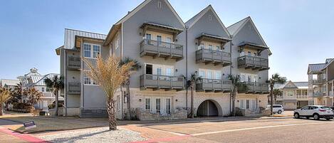 A multi-story hotel with balconies, a central entrance, and a parking area.