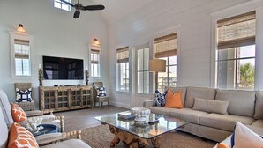 A spacious living room with a large flat-screen TV, comfortable seating, and large windows.