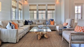 A living room with a sectional sofa, a glass coffee table, and a woven rug.