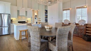 A modern kitchen with white cabinetry, a central island, and a dining area with wicker chairs and a dark table.