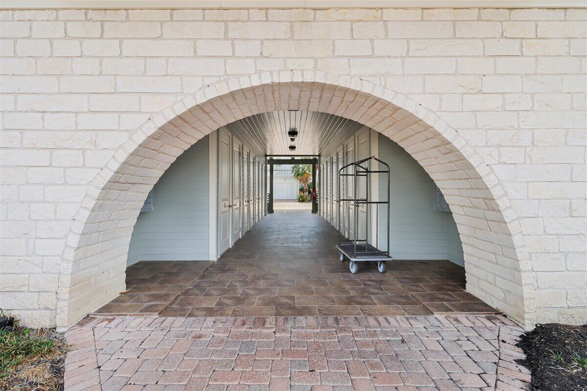 A corridor with a brick floor, white brick walls, and a metal rack with a cart.