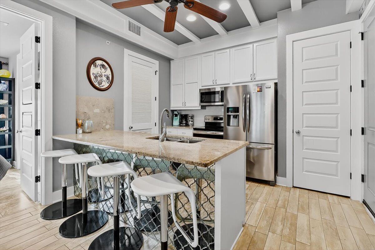 A modern kitchen with white cabinets, stainless steel appliances, a bar area with stools, and a ceiling fan.