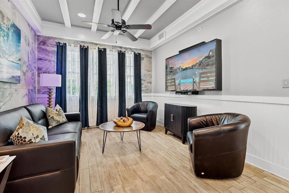 Una sala de estar con un sofá, dos sillones, una mesa de centro y un televisor en la pared.