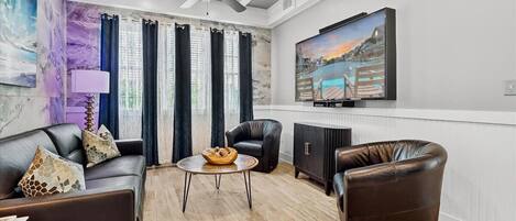 Una sala de estar con un sofá, dos sillones, una mesa de centro y un televisor en la pared.