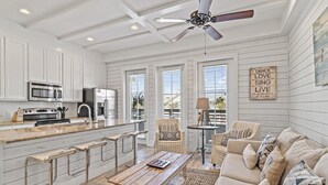 A spacious kitchen with white cabinetry, a central island with bar stools, and a dining area with a wooden table and cushioned seating. - Nautical Launch TC 1207 (Port Aransas)