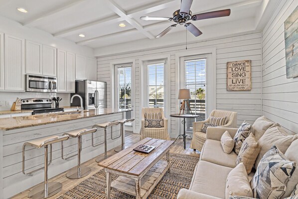 A spacious kitchen with white cabinetry, a central island with bar stools, and a dining area with a wooden table and cushioned seating. - Nautical Launch TC 1207 (Port Aransas)