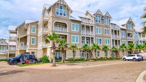 A multi-story hotel with balconies, palm trees, and a parking area. - Almost Heaven TC 2201 (Port Aransas)