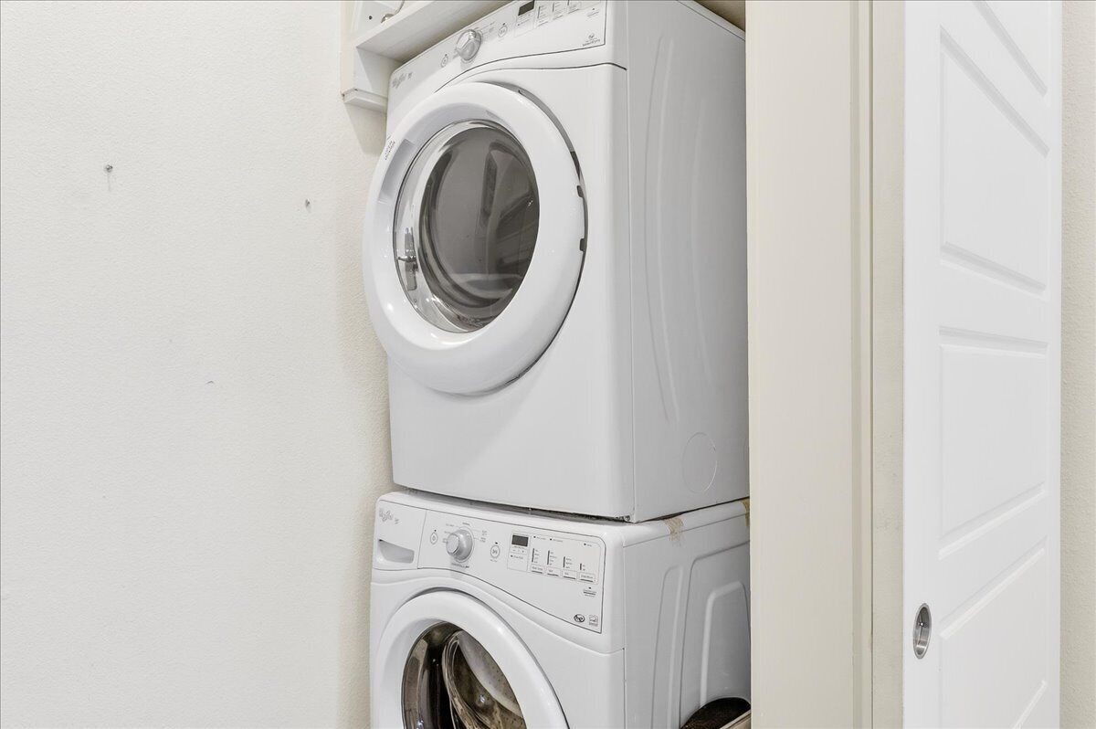 Een gestapelde wasmachine en droger in een ruimte met een effen muur en een deur.