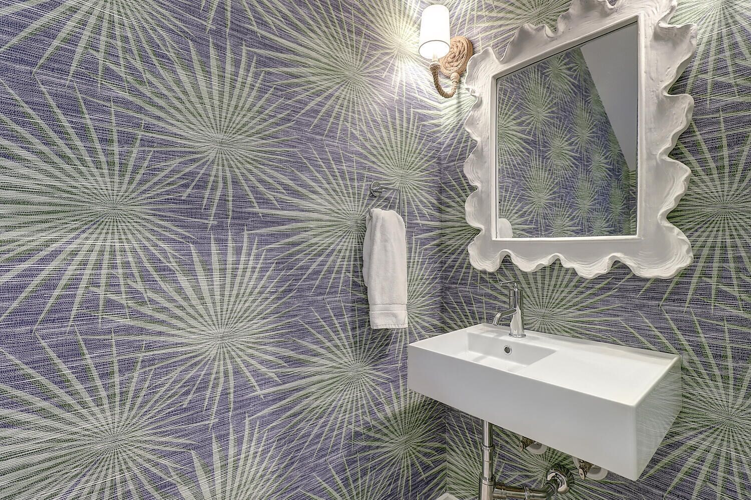 Une salle de bain avec un lavabo blanc, un miroir doté d’un cadre ondulé et une serviette accrochée au mur.