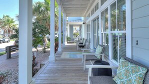 A covered porch with outdoor seating, palm trees, and a view of the street. - Lollygag 107 ST (Port Aransas)