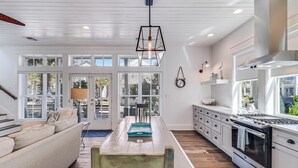 A modern kitchen with a dining area, large windows, and a staircase. - Lollygag 107 ST (Port Aransas)