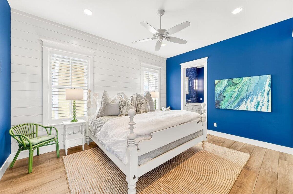 A bedroom with a white bed, a ceiling fan, a green chair, and a blue wall.