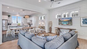 A modern kitchen with white cabinets, a dining area with a wooden table and chairs, and a living room with a gray sofa and striped pillows. - One Particular Harbor 119 FI (Port Aransas)