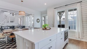 A modern kitchen with white cabinetry, a large island, and a dining area with a sofa and wooden table. - One Particular Harbor 119 FI (Port Aransas)