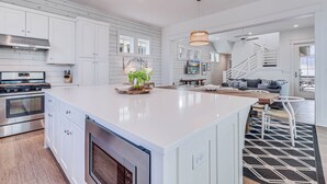A modern kitchen with white cabinetry, a large island, stainless steel appliances, and a dining area with a staircase. - One Particular Harbor 119 FI (Port Aransas)
